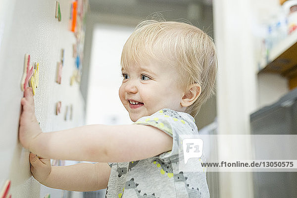 Lächelnder kleiner Junge spielt zu Hause mit bunten Magnetbuchstaben auf Metallschrank