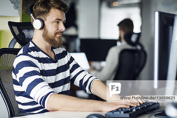 Businessman listening music while using computer in creative office