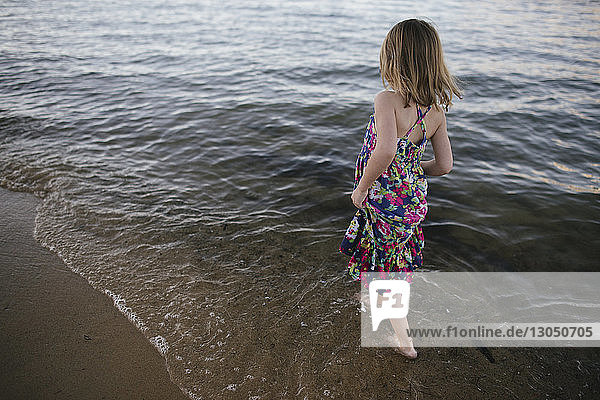 Rückansicht eines sorglosen Mädchens  das am Strand im Meer spazieren geht
