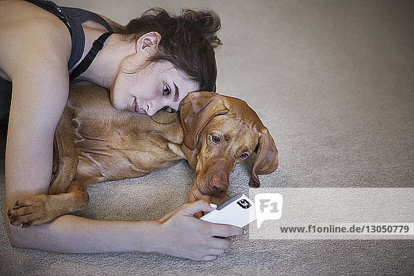 Schrägaufnahme einer Frau mit Hund  die sich im Liegen auf dem Teppich zu Hause selbstständig macht