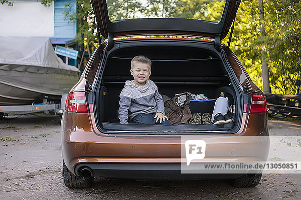 Porträt eines glücklichen Jungen  der im Kofferraum eines Autos sitzt