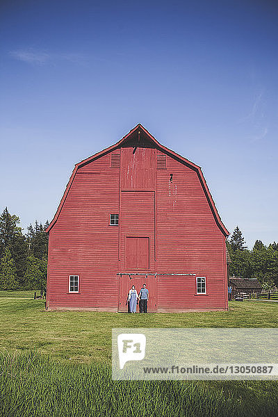 Mann und Frau stehen auf Grasfeld gegen rote Scheune im Campbell Valley Regional Park gegen den Himmel