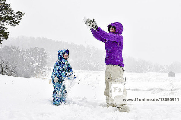 Mutter und Tochter spielen mit Schnee  während sie auf dem Feld gegen den Himmel stehen