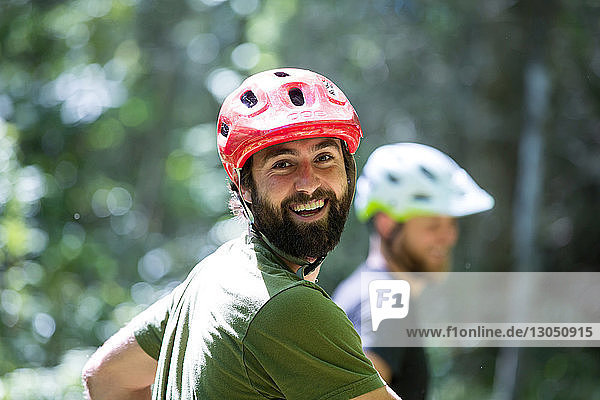 Porträt eines glücklichen Wanderers mit Fahrradhelm und Freund im Hintergrund