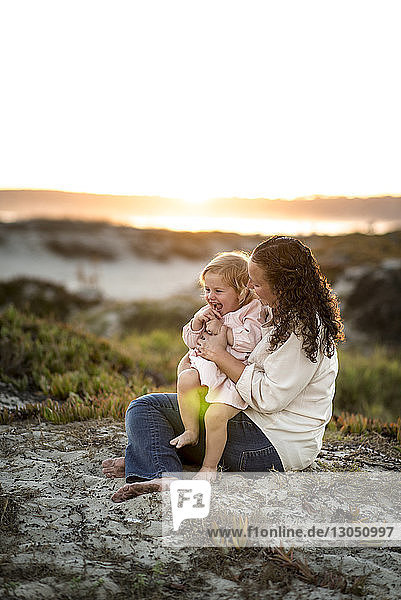 Mother and daughter sitting on sand against sky