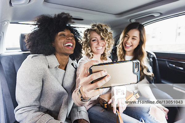 Fröhliche Geschäftsfrauen  die im Auto sitzen und sich mit einem Smartphone selbstständig machen