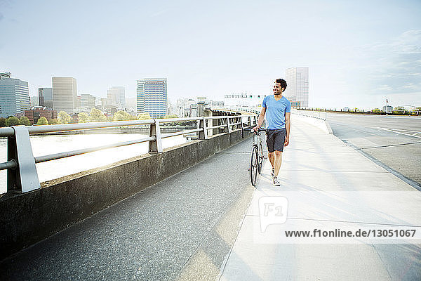 Männlicher Athlet zu Fuß mit dem Fahrrad auf einem Fußweg in der Stadt
