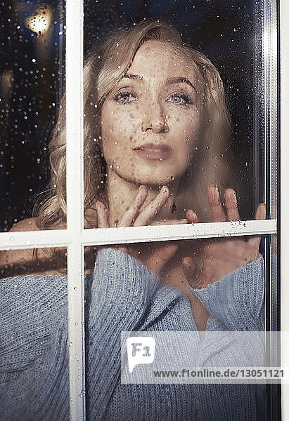 Porträt einer selbstbewussten Frau durch nasses Fenster zu Hause gesehen