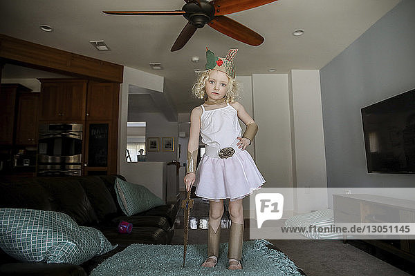 Portrait of confident girl in crown holding sword at home