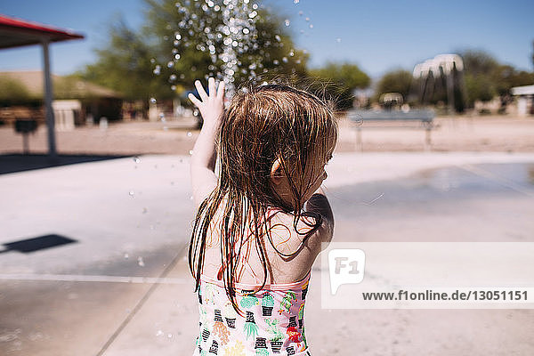 Playful girl playing with water in park during summer