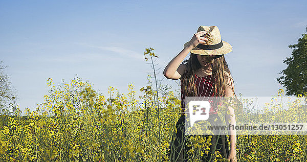 Teenagermädchen trägt Hut  während sie am sonnigen Tag auf dem Feld vor blauem Himmel steht
