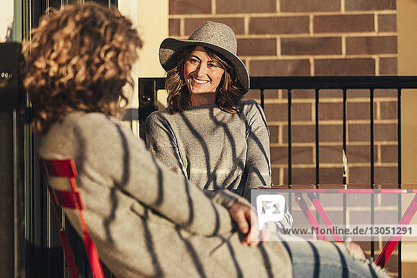 Lächelnde Geschäftsfrau schaut eine Kollegin an  die auf dem Hotelbalkon sitzt