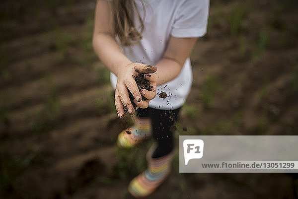 Low section of girl holding soil while standing on field
