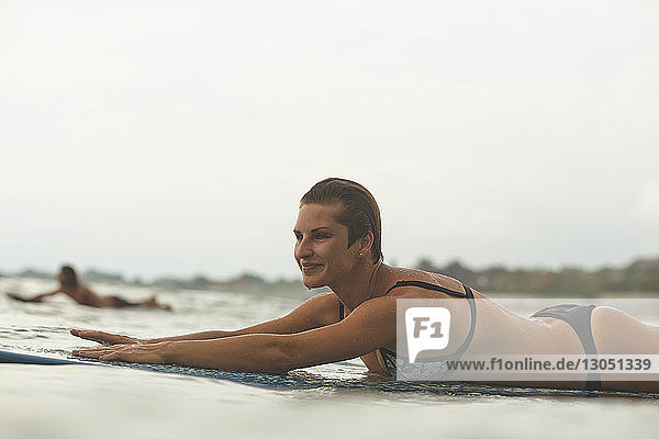 Confident woman lying on surfboard in sea against clear sky