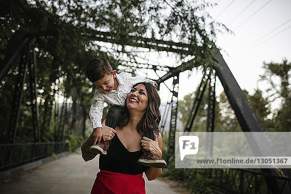 Cheerful mother carrying son on shoulders at bridge