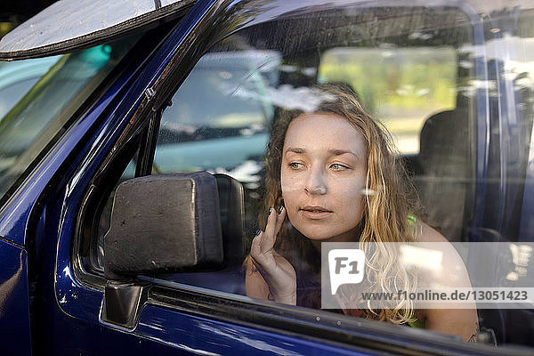 Woman touching cheek while looking in side-view mirror of car