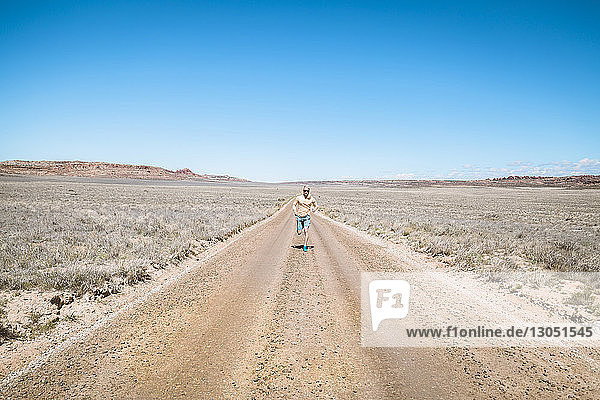 Mid distance of man running on dirt road amidst landscape against clear blue sky
