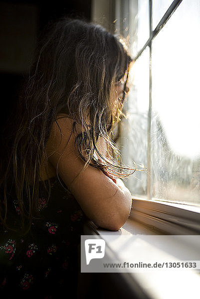 Seitenansicht eines nachdenklichen Mädchens  das zu Hause durchs Fenster schaut