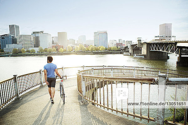 Rückansicht eines männlichen Athleten  der auf einer Brücke am Fluss in der Stadt läuft