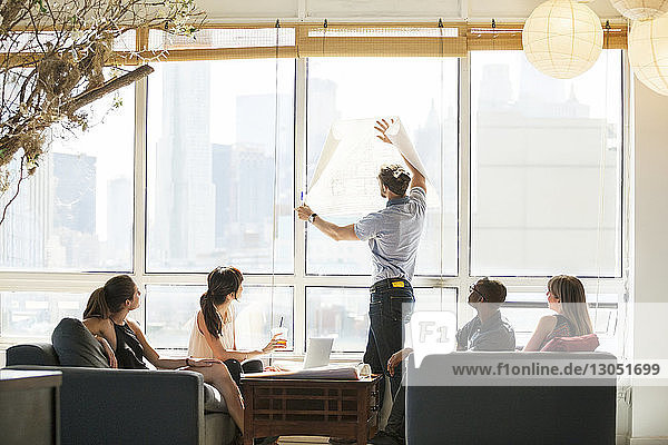Businessman holding blueprint against window during meeting
