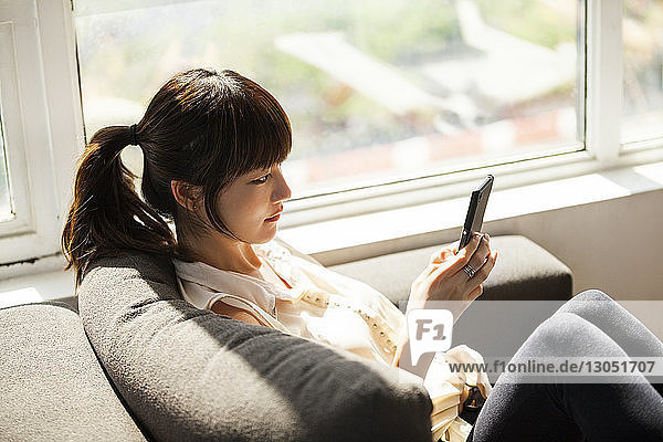 Seitenansicht einer Geschäftsfrau  die ein Smartphone auf dem Sofa im Kreativbüro benutzt