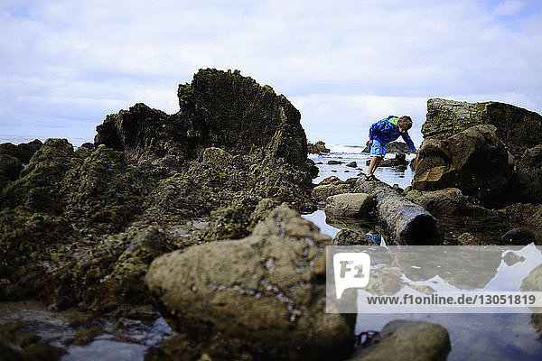 Boy searching something while standing on rocks at Laguna Beach