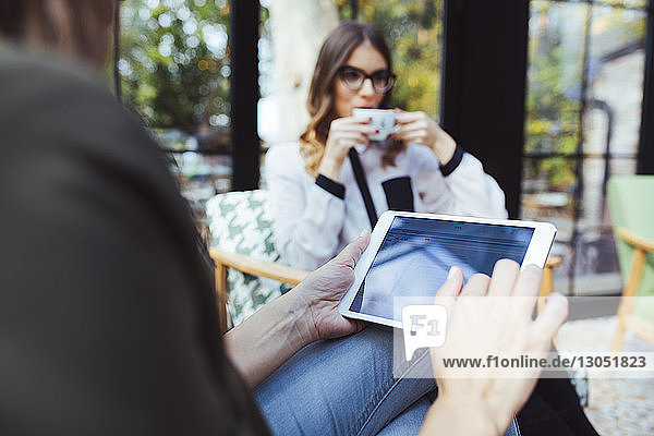 Mittelsektion einer Frau  die einen Tablet-Computer benutzt  während ein Kollege im Café Kaffee trinkt