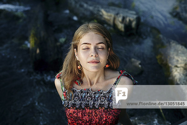 Hochwinkelansicht einer auf Felsen sitzenden Frau mit geschlossenen Augen