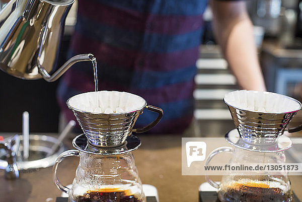 Barista pouring boiling water into coffee filter at cafe