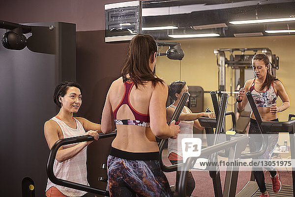 Lächelnde Frau betrachtet Freundin  die im Fitnessstudio auf dem Laufband vor dem Spiegel läuft