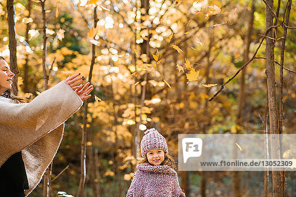 Mutter und Tochter werfen Herbstblätter im Wald in die Luft