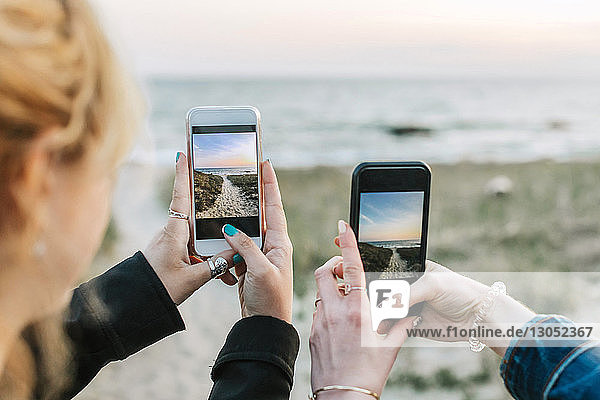 Zwei junge Frauen fotografieren den Strand mit Smartphones, über die Schulter gesehen, Menemsha, Martha's Vineyard, Massachusetts, USA