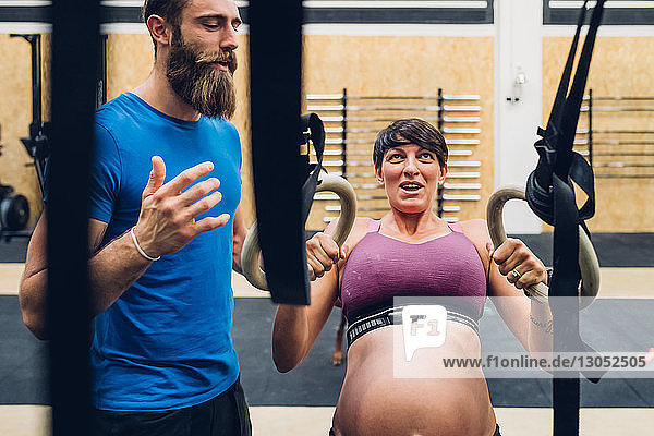 Trainer guiding pregnant woman using exercise equipment in gym
