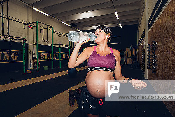 Schwangere Frau trinkt aus Wasserflasche im Fitnessstudio