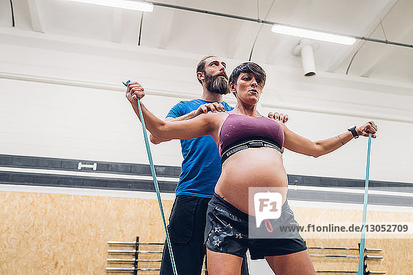 Trainerin  die schwangere Frau bei der Benutzung von Seilen im Fitnessstudio führt