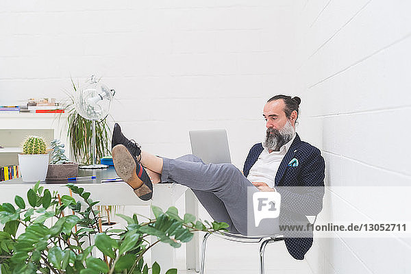 Cool businessman with feet up in office looking at laptop
