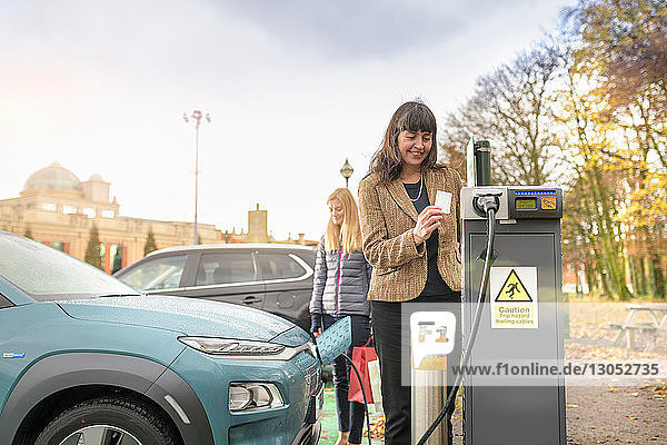 Female shoppers charging electric car at charge point Manchester UK