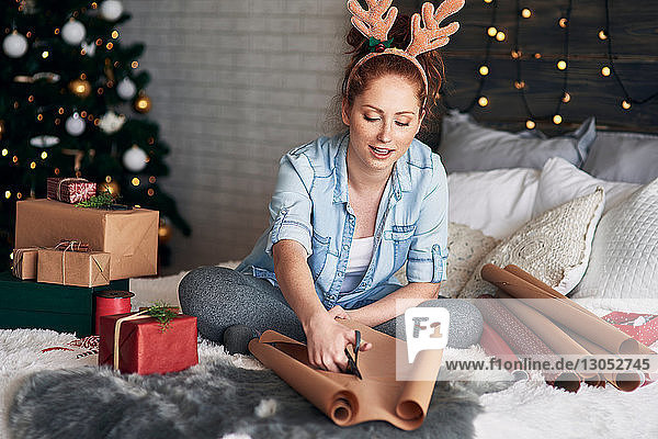 Woman wrapping Christmas presents on bed