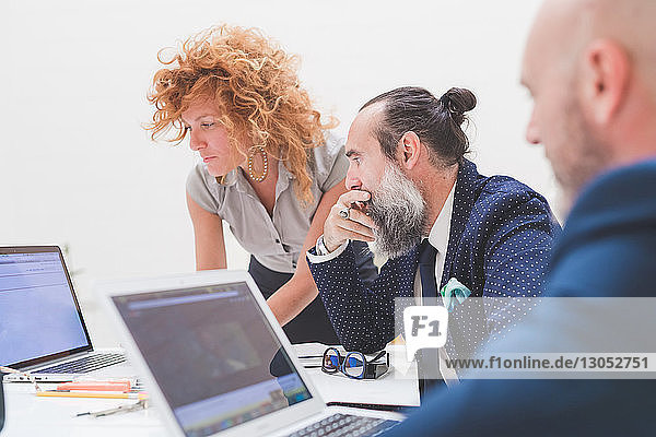 Businesswoman and men looking at laptop on office desk  over shoulder view