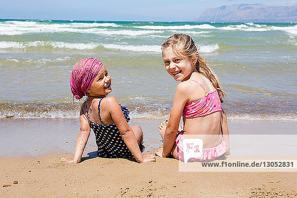Zwei Mädchen sitzen am Strand und blicken zurück  Porträt  Castellammare del Golfo  Sizilien  Italien