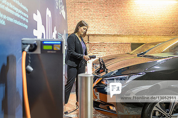 Geschäftsfrau, die ihr Auto an einer Ladestation für Elektrofahrzeuge anschließt, Manchester, UK