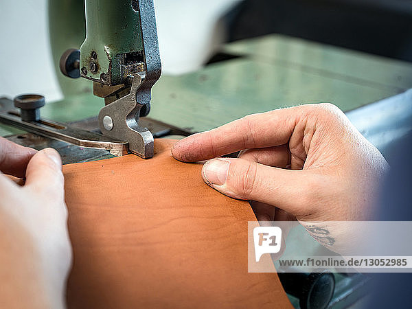 Lederarbeiter bei der Bearbeitung der Handtaschenkante aus Leder in der Werkstatt  Nahaufnahme der Hände