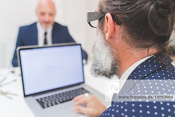 Businessman using laptop at office desk  over shoulder view