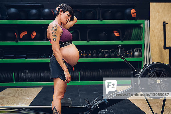 Schwangere Frau betrachtet Rudergerät im Fitnessstudio