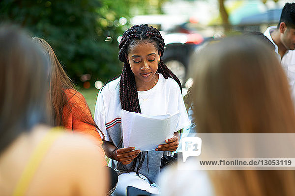 Männlicher und weiblicher Hochschulstudent betrachten Papierkram auf dem Rasen des College-Campus  Blick über die Schulter