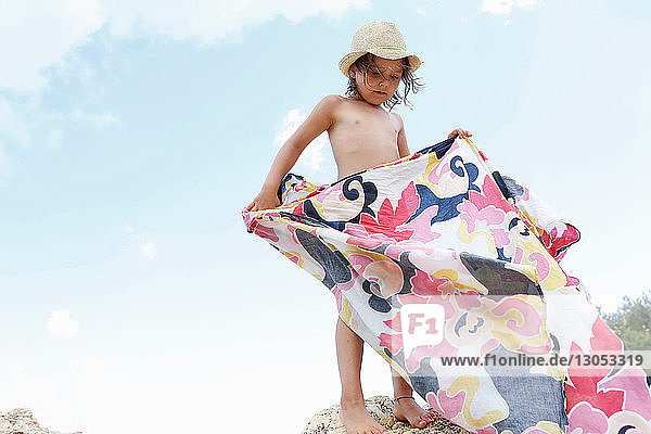 Girl standing on rock folding patterned blanket  Scopello  Sicily  Italy