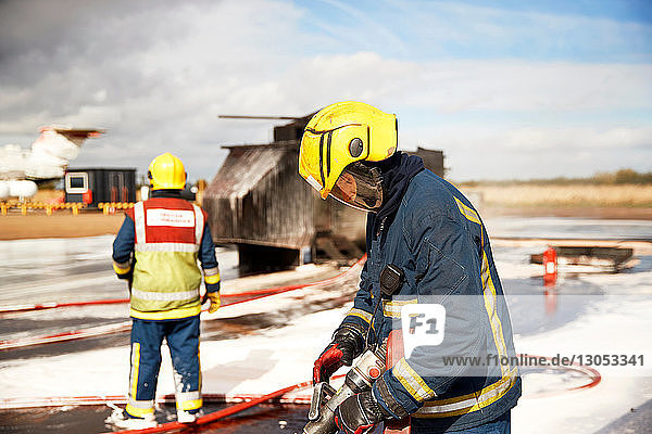 Ausbildung von Feuerwehrleuten  Feuerwehrmänner überprüfen Feuerwehrschlauch nach dem Schein-Hubschrauber-Feuer in Trainingsanlage