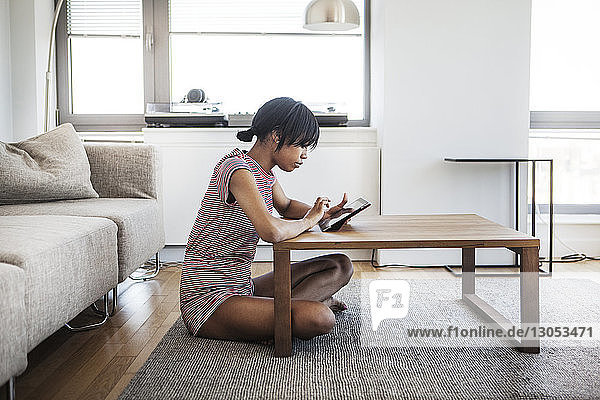 Seitenansicht einer Frau  die zu Hause einen Tablet-Computer am Tisch benutzt