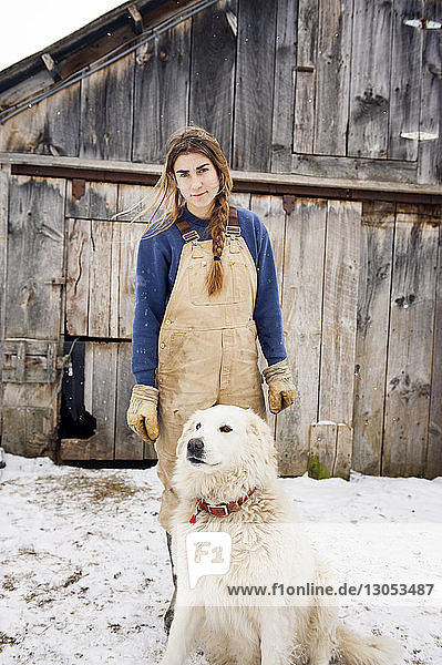 Porträt einer Frau  die neben einem Hund vor einer Scheune auf einem schneebedeckten Feld steht