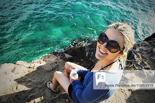 Hochwinkelansicht einer lächelnden Frau  die auf einem Felsen am Fluss sitzt